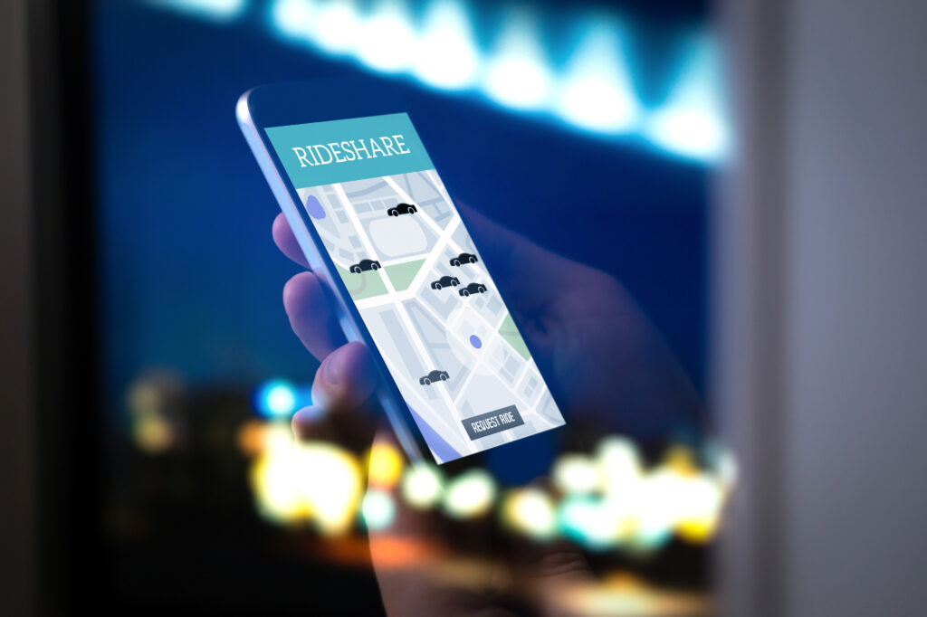 Ride sharing and carpool mobile application. Rideshare taxi app on smartphone screen. Modern online people and commuter transportation service. Man holding phone late at night. Huntington Beach street lights.