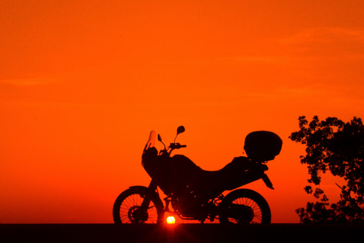 dark motorcycle silhouette in the forefront of deep orange sunset